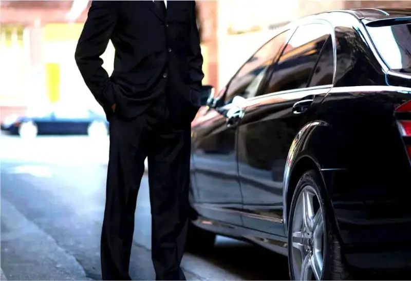 hombre chófer traje elegante negro junto a vehiculo de gama alta esperando al cliente